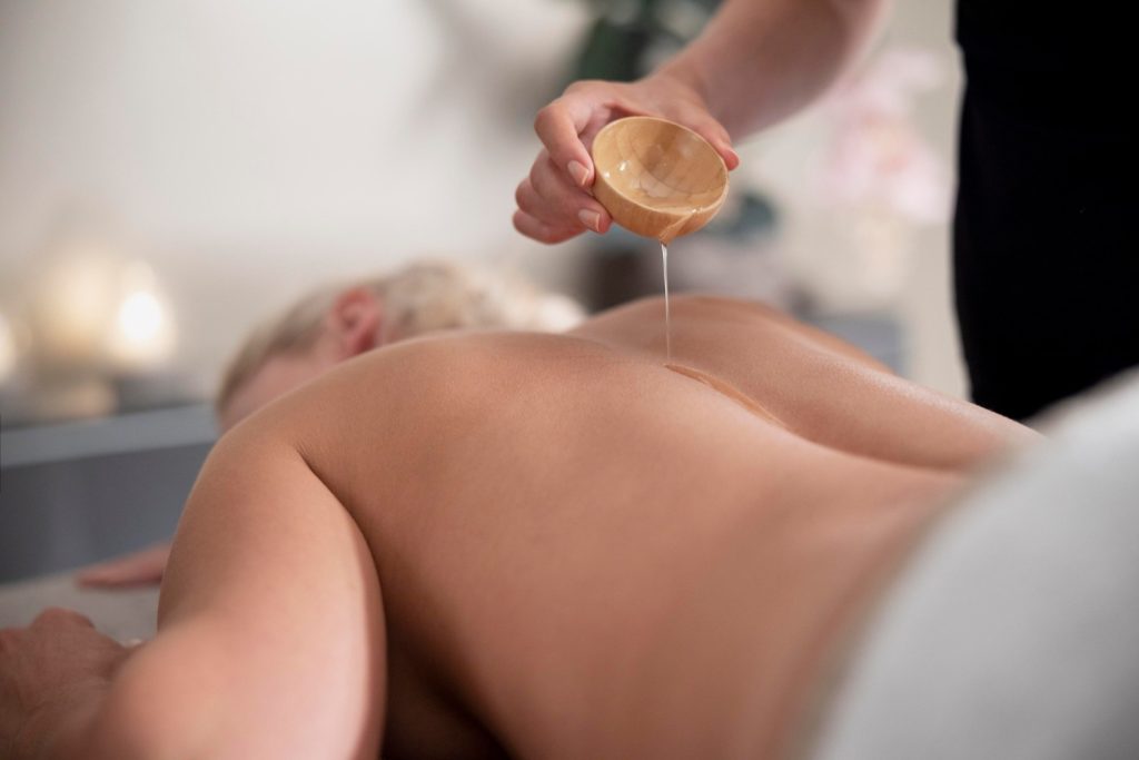 masseurin-giesst-warmes-ol-auf-den-rucken-einer-liegenden-person-in-ruhiger-wellness-umgebung-sanfte-behandlung-mit-fokus-auf-entspannung-und-pflege