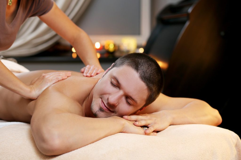 mann-liegt-entspannt-auf-massageliege-wahrend-einer-thai-olmassage-masseurin-massiert-den-rucken-ruhige-warme-atmosphare-mit-kerzenlicht-und-entspannung