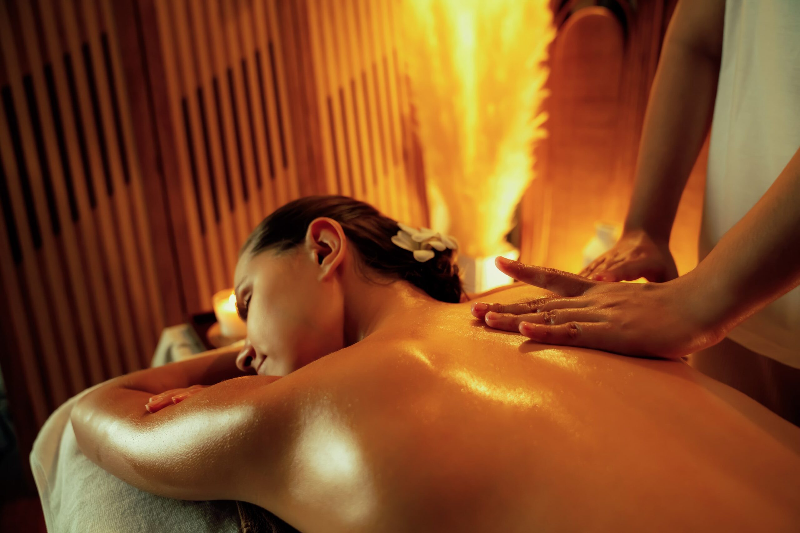 frau-liegt-auf-massagetisch-mit-geschlossenen-augen-masseurin-fuhrt-eine-ruckenmassage-mit-warmem-ol-durch-warmer-lichtdurchfluteter-raum-mit-sanfter-beleuchtung-und-gefuhl-tiefer-entspannung